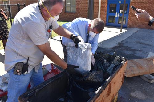 Two school officials in masks and gloves retrieving items from time capsule 